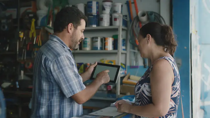 Dono de loja de material de construção mostrando um tablet a uma cliente no balcão