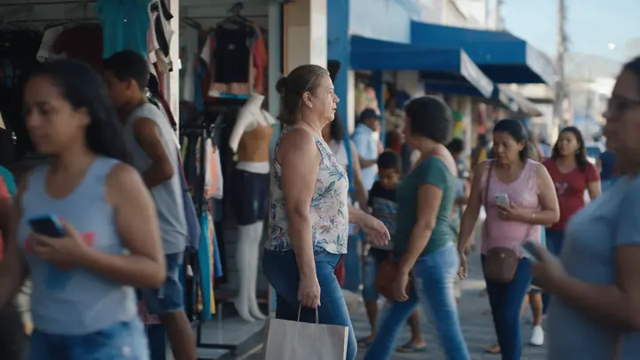 Mulher saindo de uma loja de roupas com uma sacola numa rua comercial movimentada do interior