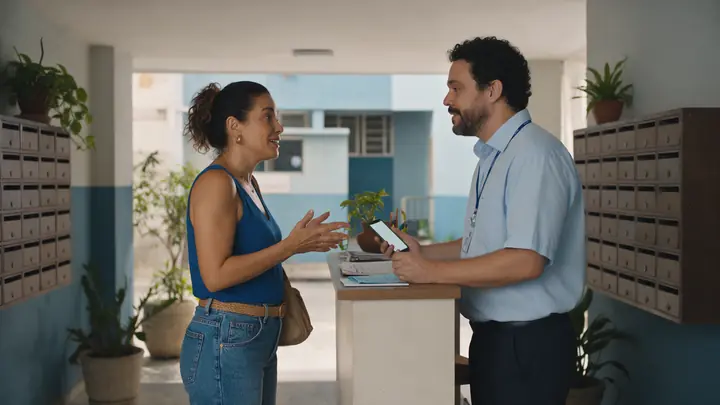 Moradora conversando com o síndico no balcão da portaria de um prédio residencial simples