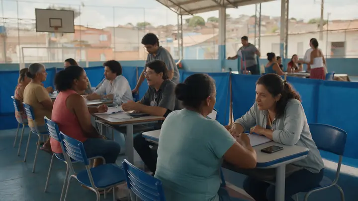 Pessoas sendo atendidas em mesas simples num mutirão de negociação de dívidas em quadra coberta