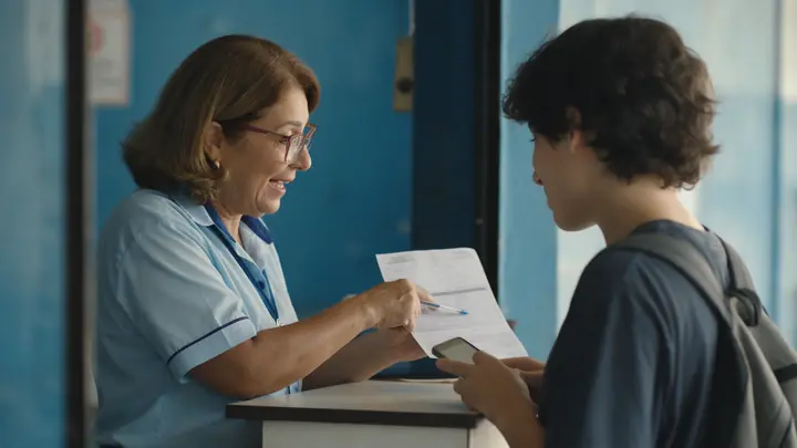 Atendente explicando com calma um papel impresso a uma jovem cliente no balcão de atendimento