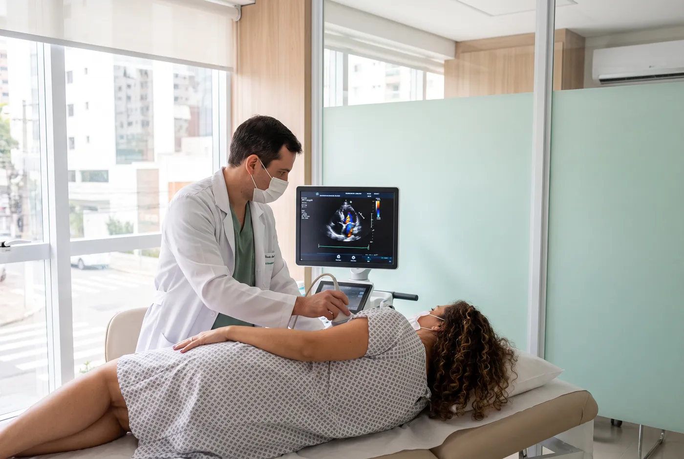 Médico faz ecocardiograma em paciente deitada de lado, observando o coração no monitor