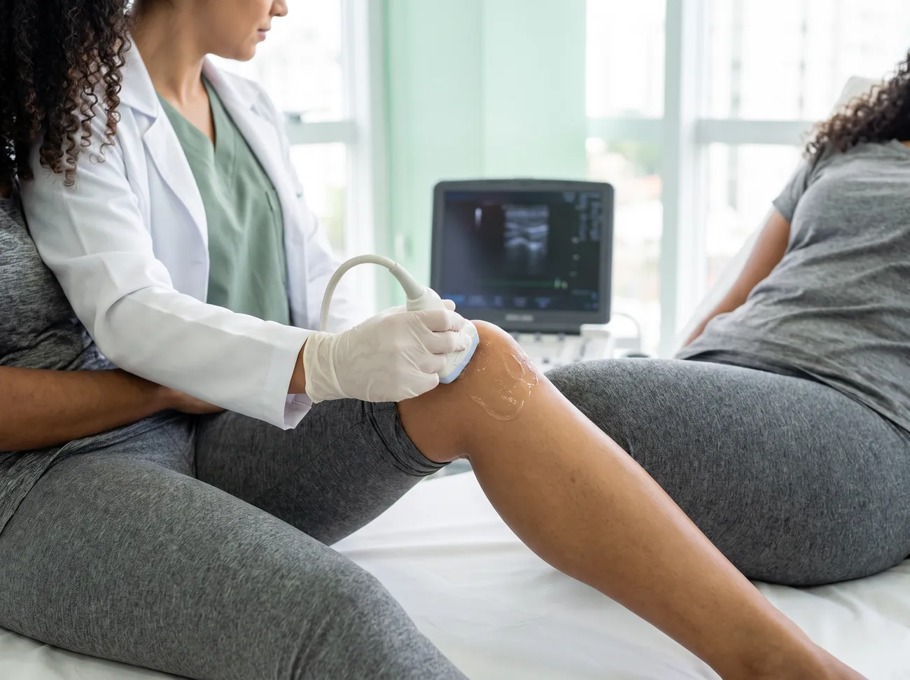 Médica examina o joelho de uma paciente com o transdutor do ultrassom