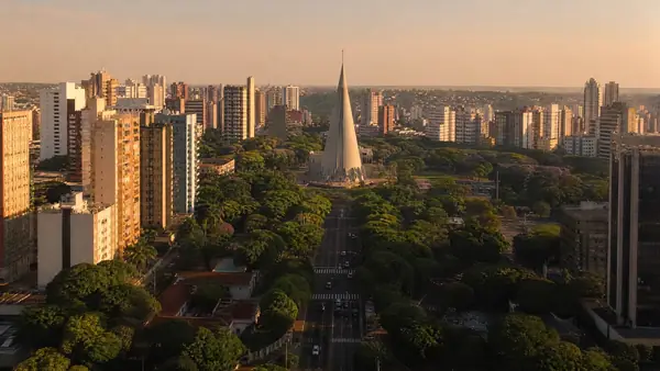 Vista de Maringá ao entardecer, com prédios, avenida arborizada e a catedral em forma de cone (imagem ilustrativa)