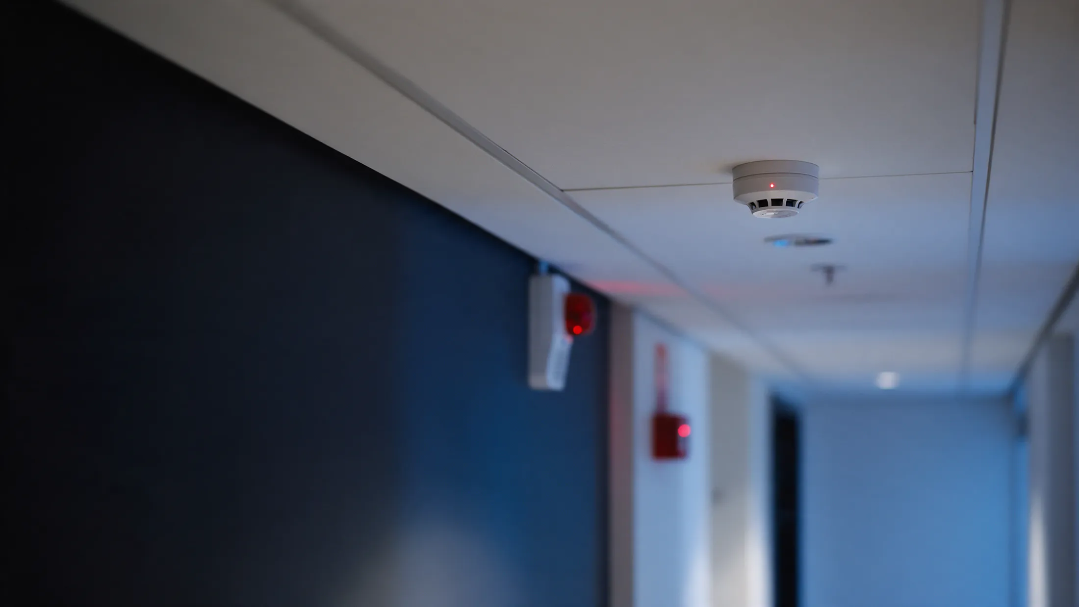 Detector de fumaça no teto de um corredor comercial, com acionador manual e sirene ao fundo