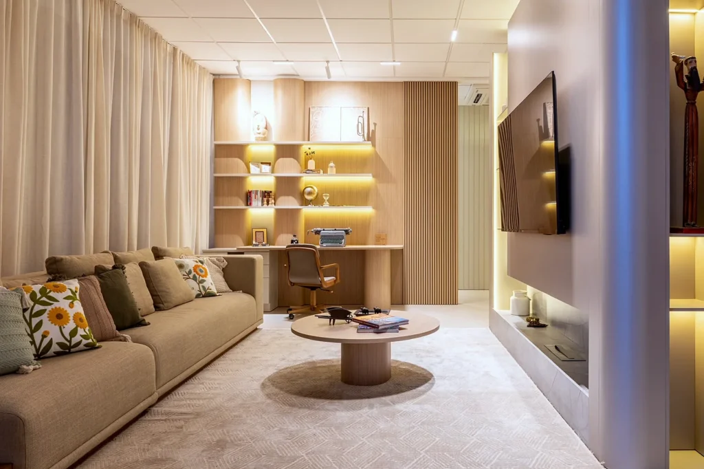 Sala de estar com estante iluminada e home office integrado ao fundo