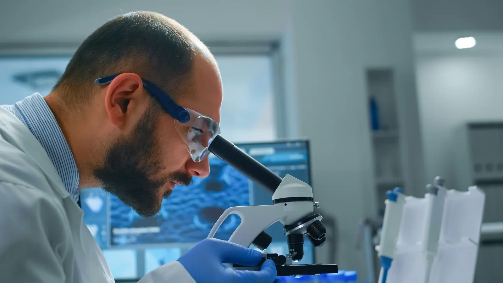 Patologista analisando lâmina no microscópio com imagem digital ao fundo