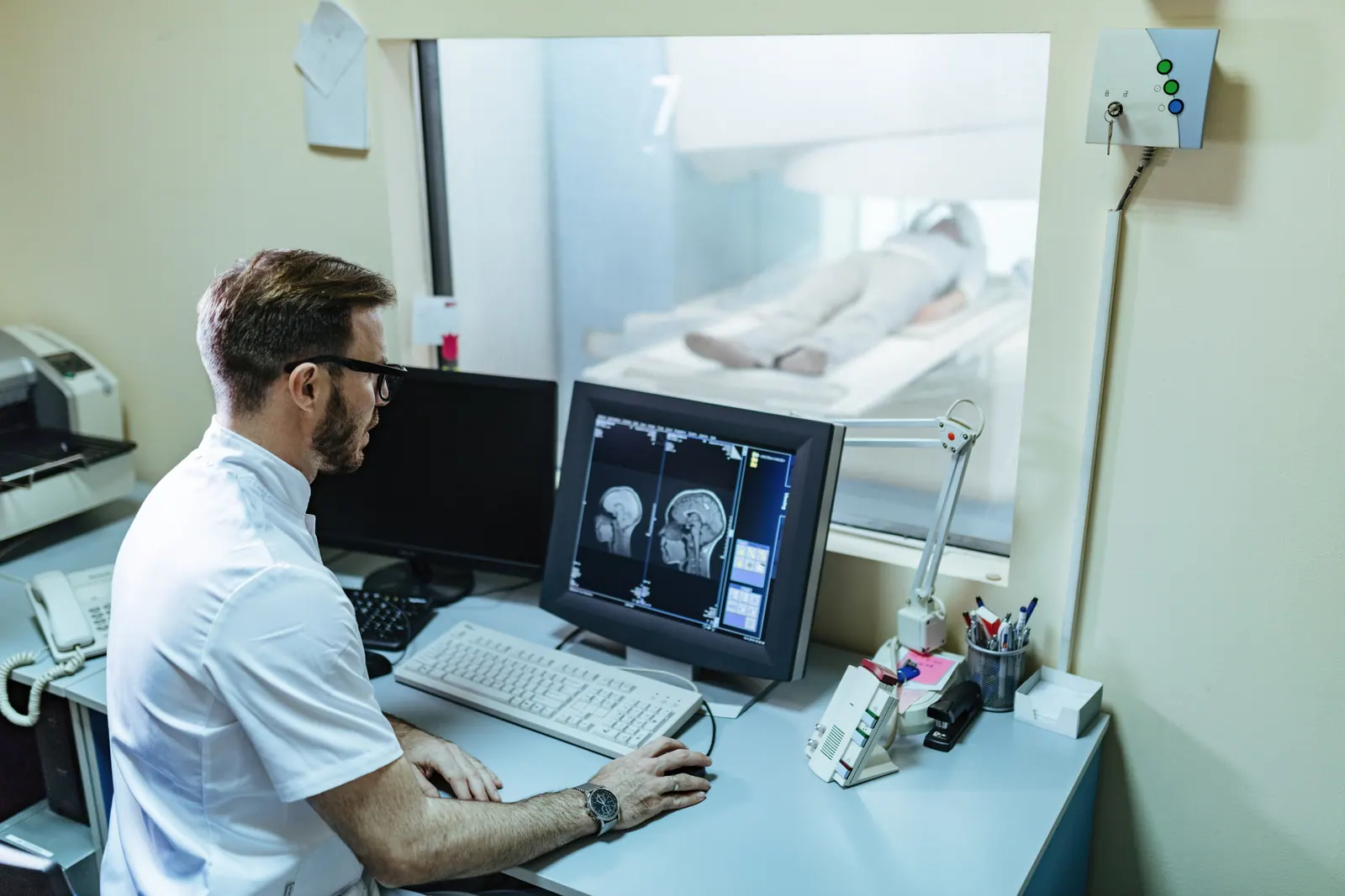 Médico radiologista acompanhando exame de ressonância magnética na sala de comando