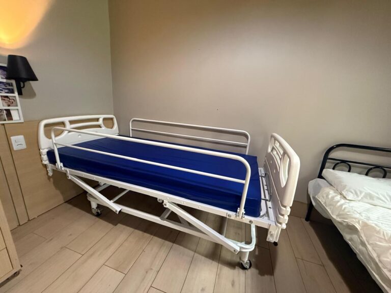 Cama hospitalar montada em quarto, com grades laterais e colchão azul
