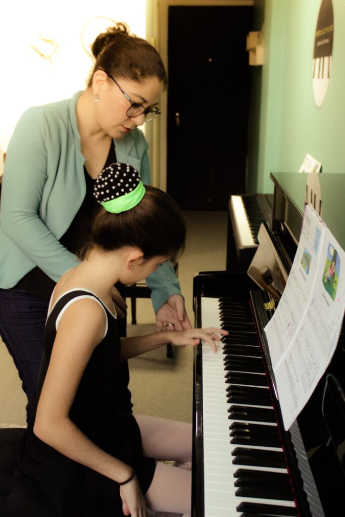 Professora ajustando a postura de aluna ao piano
