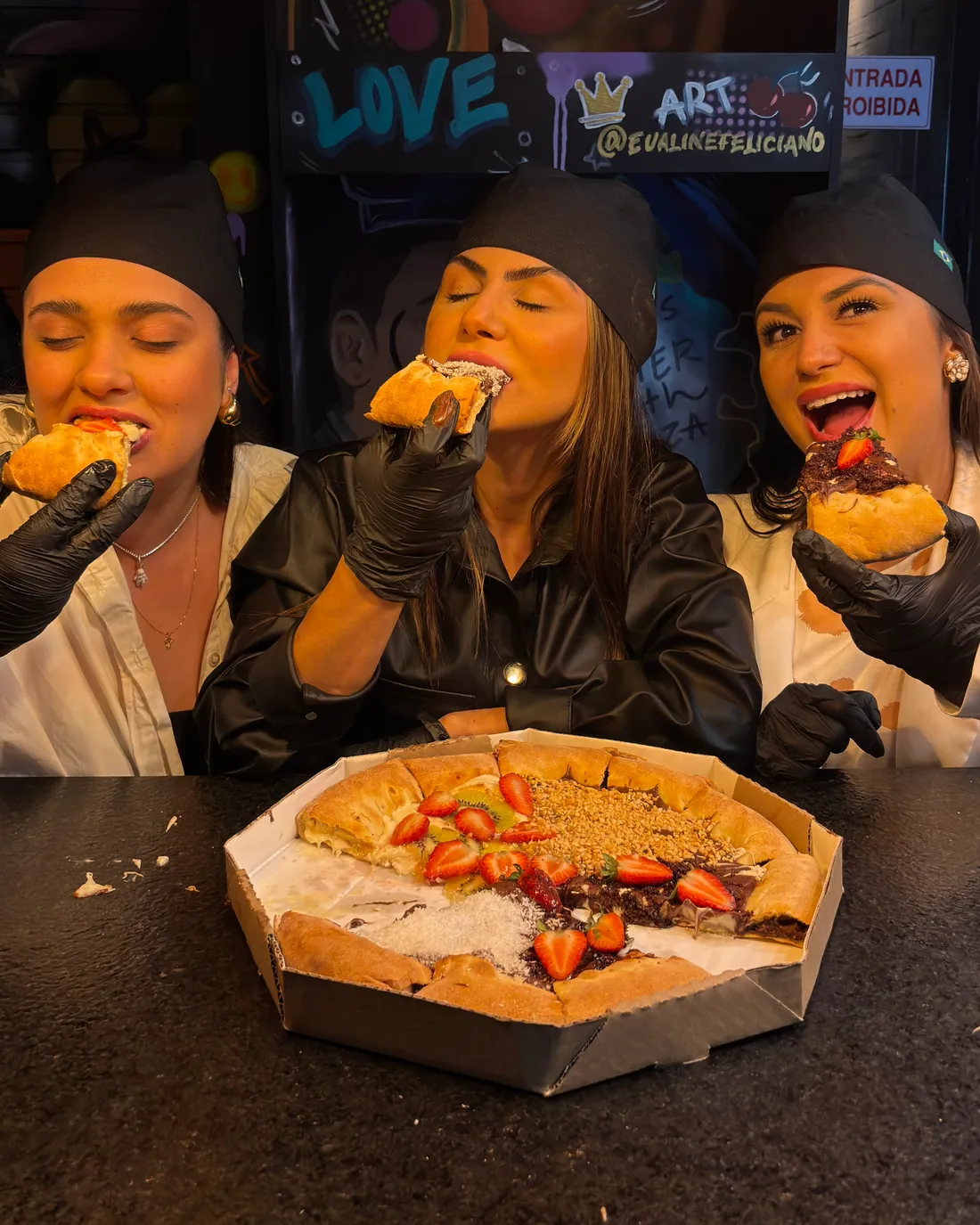Amigas comendo pizza doce no balcão do salão com arte urbana