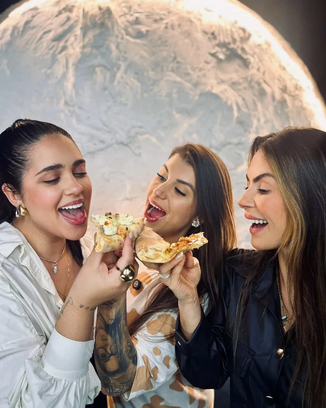 Amigas comendo pizza no salão em frente ao painel de lua