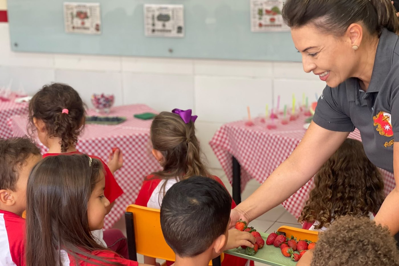 Professora oferecendo morangos a crianças da creche, em atividade de sala