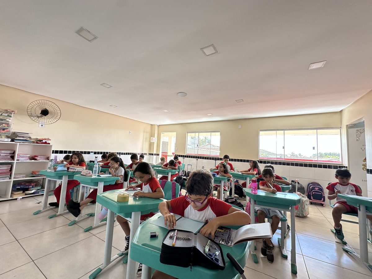 Aluno do Fundamental com o livro aberto na carteira, em sala de aula