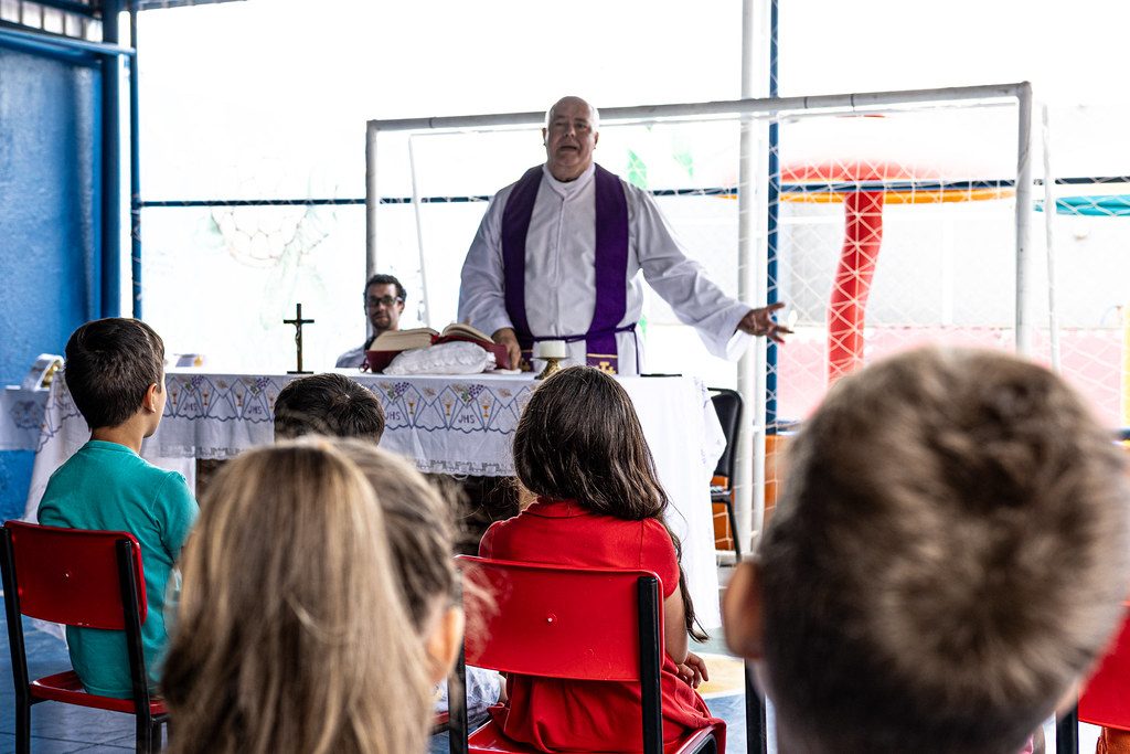 Padre conversa com alunos e famílias no pátio coberto da escola